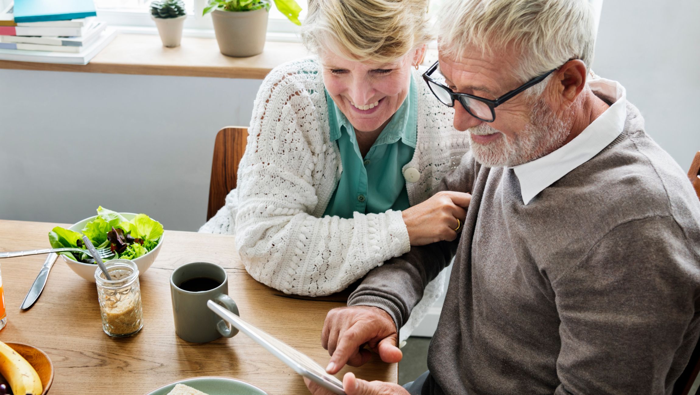 older couple sitting at a table looking at a tablet